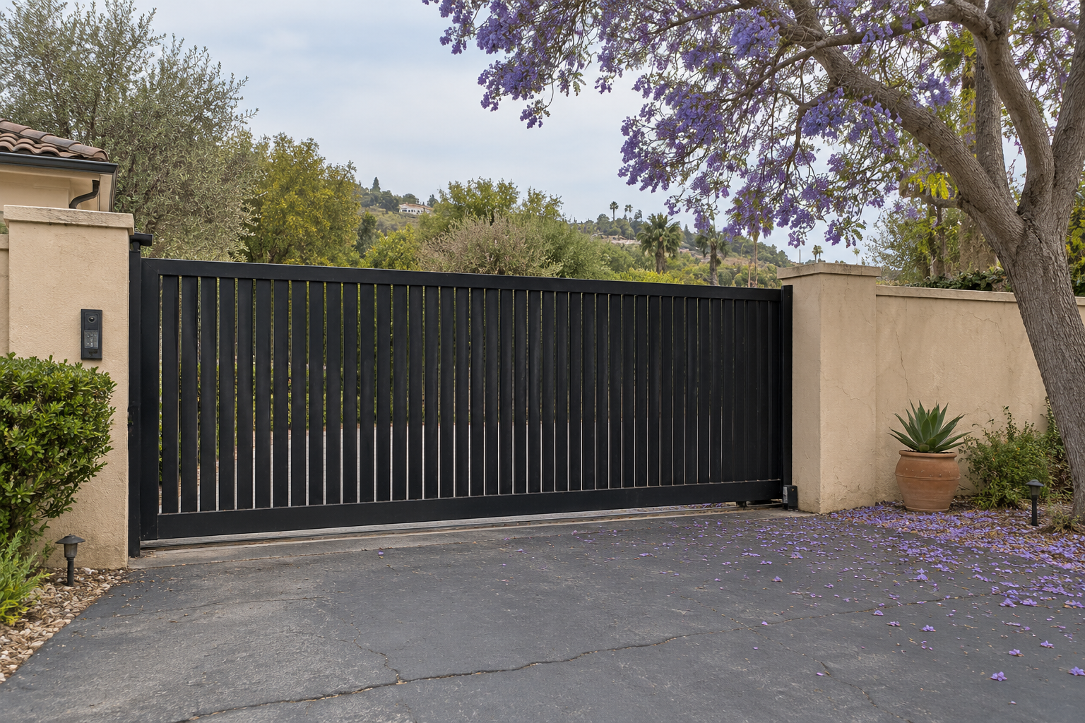 Encino electric gate repair: large black modern gate on a sunny day with blooming purple trees